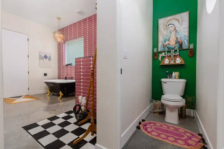 Spacious bathroom featuring a black clawfoot tub with gold-tone feet, a tiled accent wall, and a unique chandelier