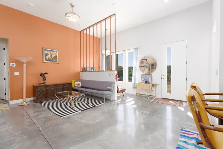 Open-concept living area featuring high ceilings, polished concrete flooring, a decorative wooden room divider, and abundant natural light from multiple windows