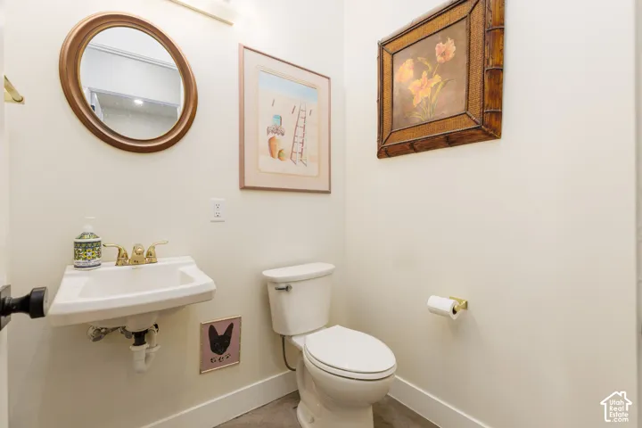 Powder room featuring a circular mirror, pedestal sink with brass-finish faucet, and a white toilet