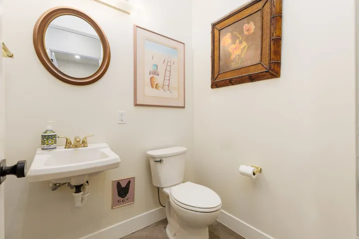 Powder room featuring a circular mirror, pedestal sink with brass-finish faucet, and a white toilet