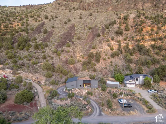 Modern gray exterior with dark trim and a contrasting wood-finish accent panel, set into a natural hillside landscape with a winding gravel driveway