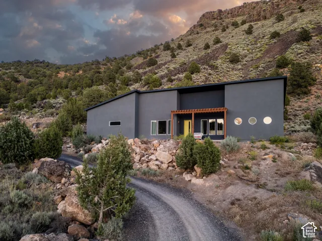 Contemporary exterior with a dark grey facade, a prominent yellow entry door, a wooden pergola, multiple circular windows, and a gravel driveway
