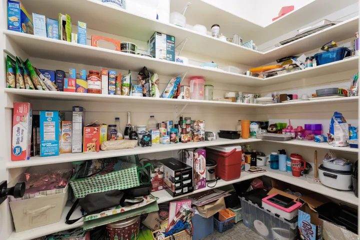 Walk-in pantry featuring extensive built-in shelving, white shelf surfaces, and white wall panels