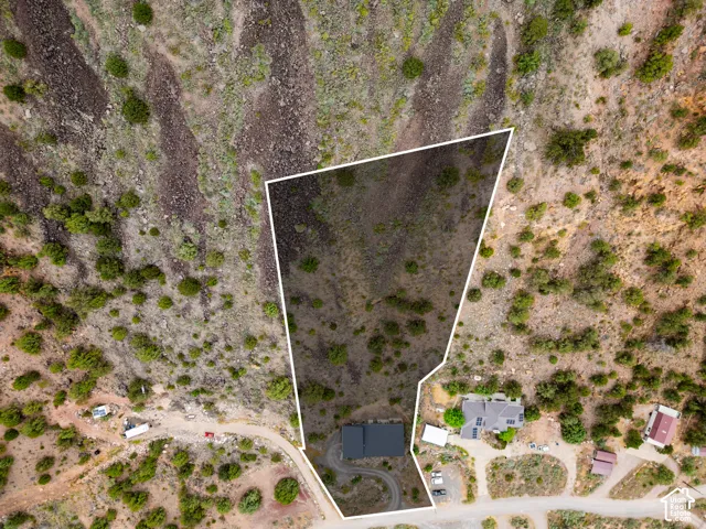 Expansive land parcel featuring a defined property boundary, natural desert landscaping, a single-story residence with a dark roof, a curved driveway, and proximity to an unpaved road