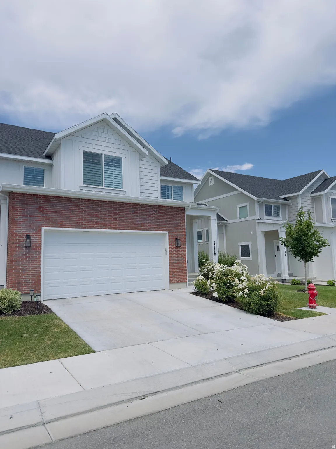 Contemporary townhome featuring a brick and white siding facade, an attached two-car garage, concrete driveway, and landscaped entry with white flowering bushes