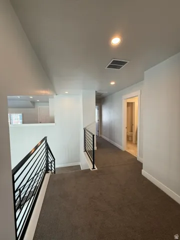 Carpeted hallway featuring recessed lighting and black metal railings