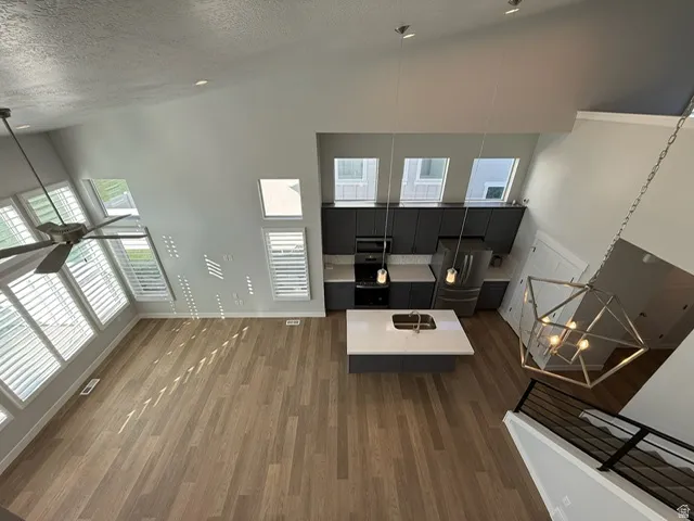 Vaulted ceilings, wood-finish flooring, modern kitchen cabinetry, integrated stainless steel appliances, and a geometric chandelier
