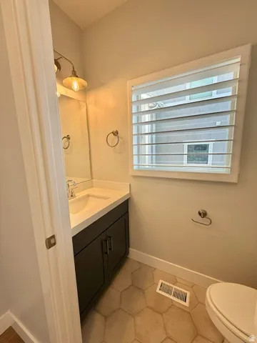 Hexagonal floor tiling, dark wood-finish vanity, integrated sink with chrome faucet, plantation shutters, and an industrial-style wall sconce
