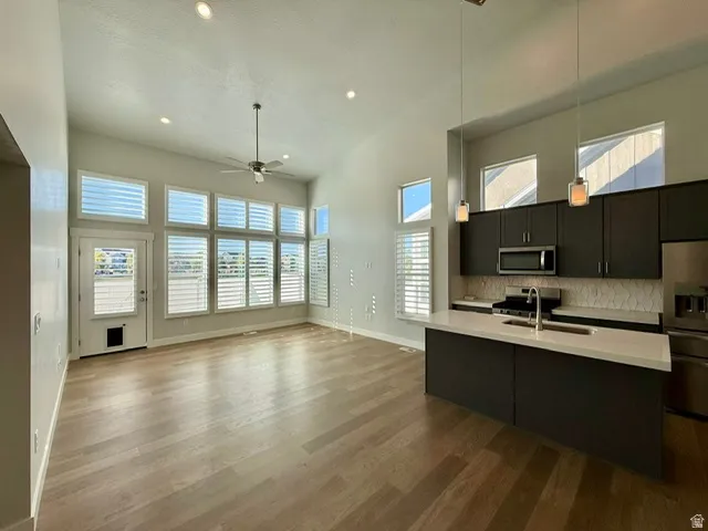 Vaulted ceilings, wood-finish flooring, recessed lighting, expansive windows with plantation shutters, and a kitchen island with pendant lighting