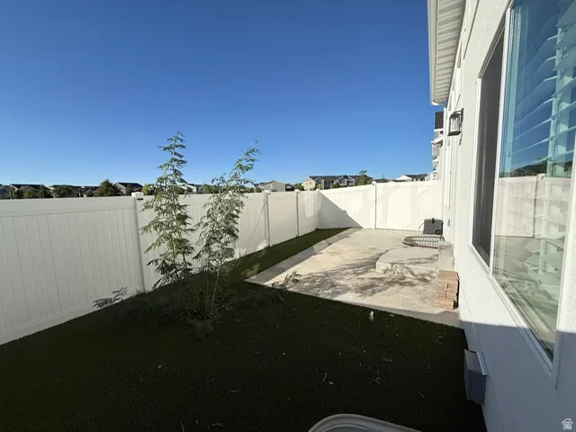 Fenced backyard with artificial turf, concrete patio, and exterior wall-mounted lighting