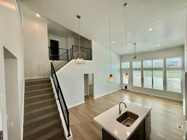 High ceilings with recessed lighting, wood-finish flooring, a kitchen island with an undermount sink, and a staircase with metal railings