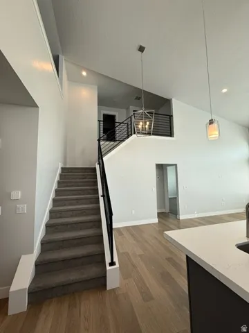 Open-concept living space with vaulted ceilings, wood-finish flooring, and a carpeted staircase featuring a contemporary metal railing