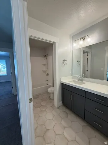 Bathroom featuring a large vanity with a white countertop, hexagon tile flooring, a bathtub with shower, and a three-light vanity fixture