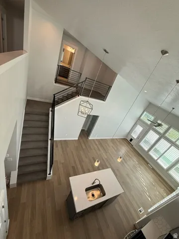 Vaulted ceilings, wood-finish flooring, kitchen island with sink and stone countertop, iron stair railing, and large windows with blinds