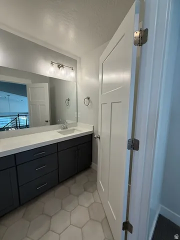 Hexagonal floor tiling, dual-tone vanity cabinetry, built-in sink, wall-mounted light fixture, and large vanity mirror