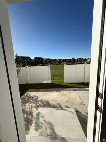 Patio area with concrete surfacing, opening to a private artificial turf yard and white privacy fencing