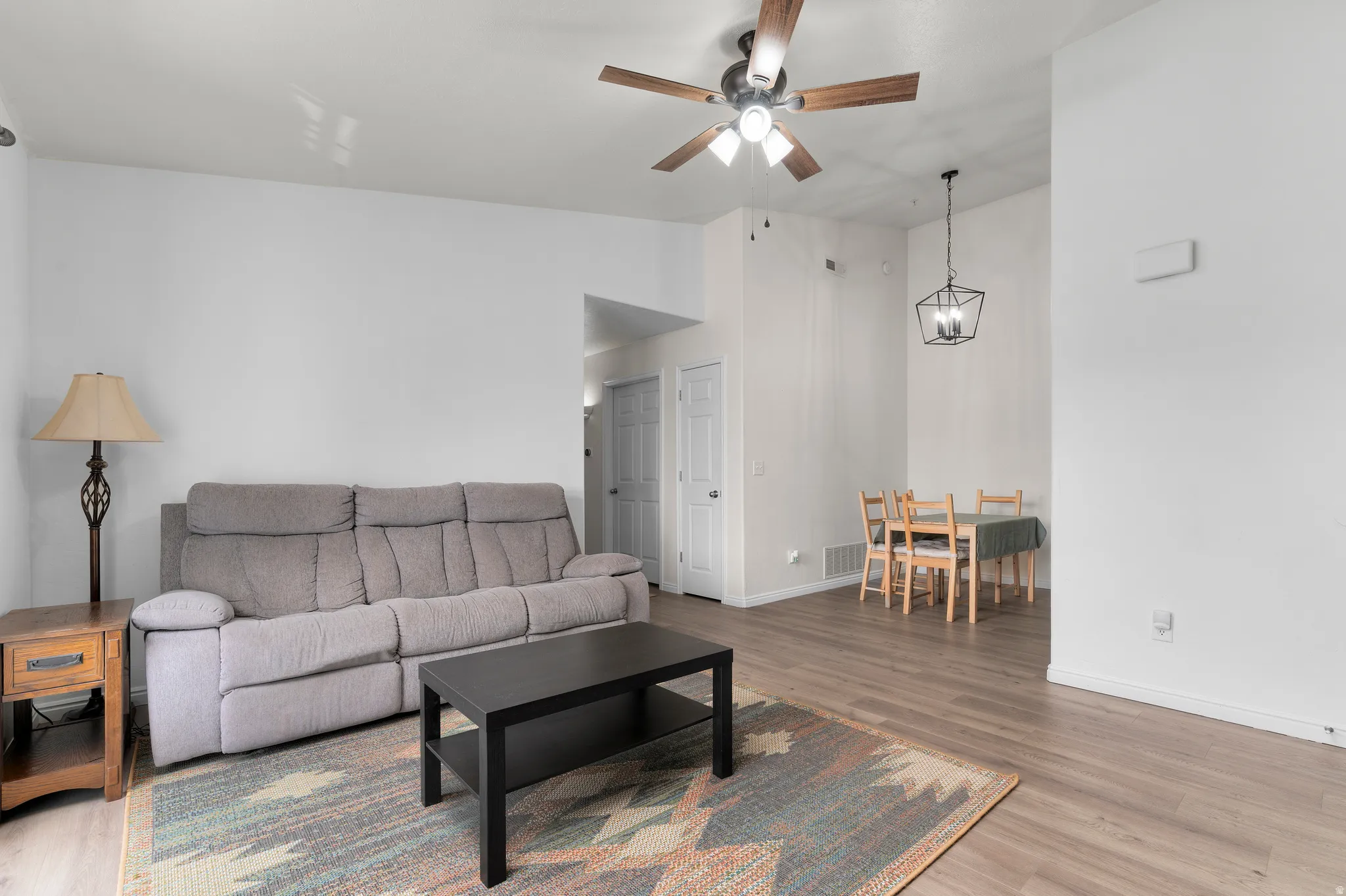 Open-concept living area featuring wood-finish flooring throughout, a vaulted ceiling with a ceiling fan, and a contemporary pendant light fixture over the dining space
