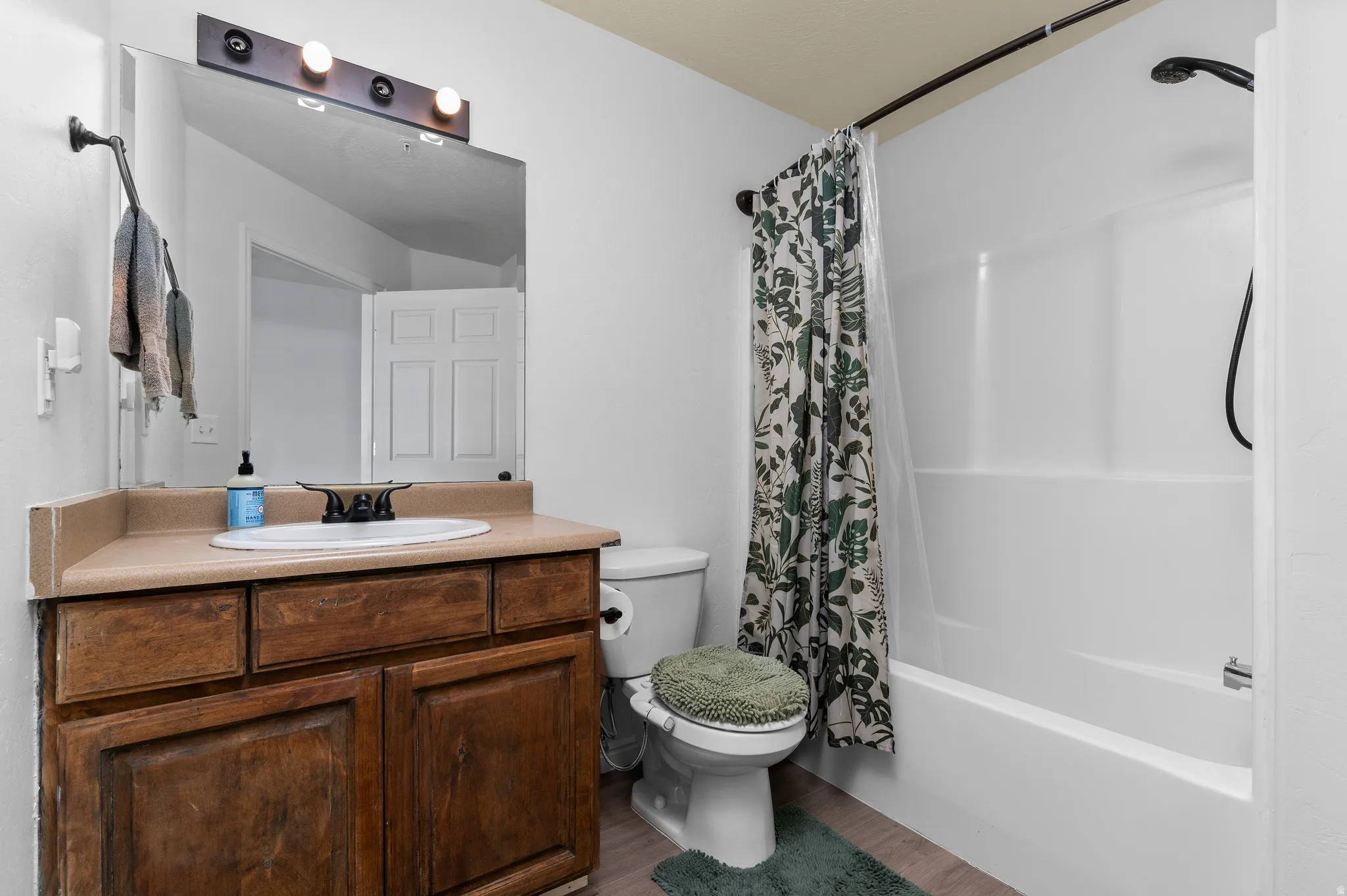 Bathroom featuring a white integrated tub and shower unit, wood-finish flooring, a vanity with a light-colored countertop, and a built-in wood vanity cabinet