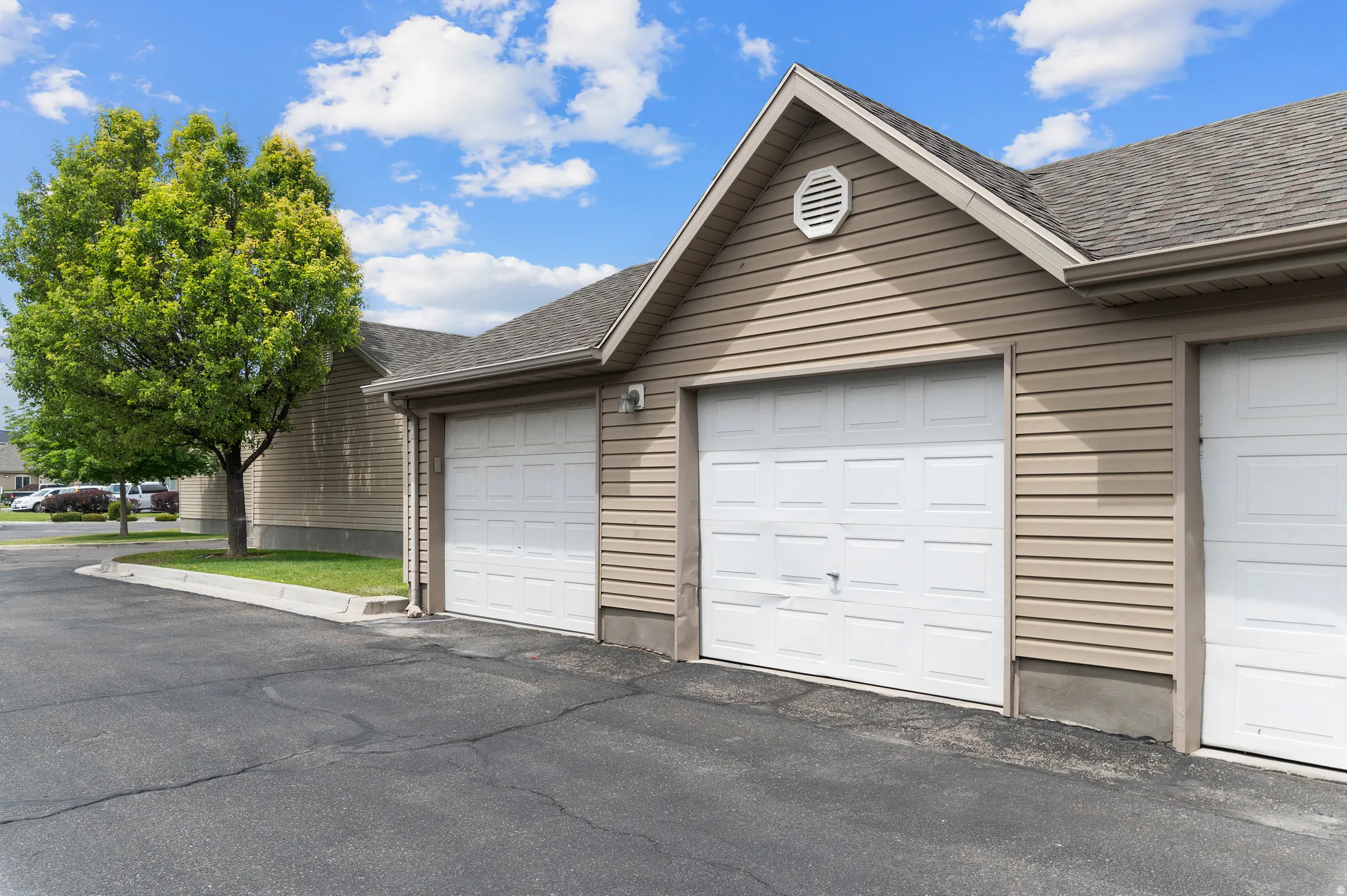 Exterior featuring light brown horizontal siding, a gray shingled roof, white paneled garage doors, and a decorative gable vent
