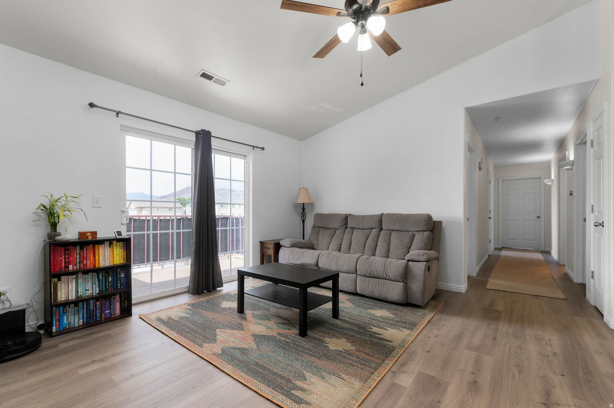 Spacious living area featuring wood-finish flooring, a sliding glass door leading to an outdoor patio, and a ceiling fan