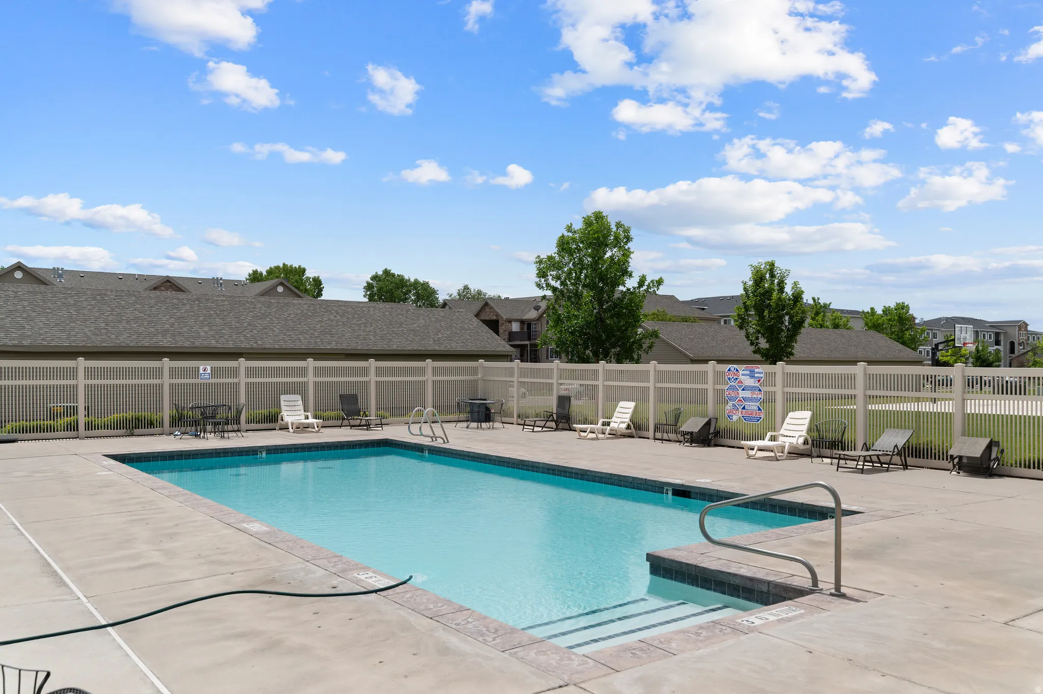 Outdoor swimming pool with a surrounding concrete deck and a light-toned privacy fence