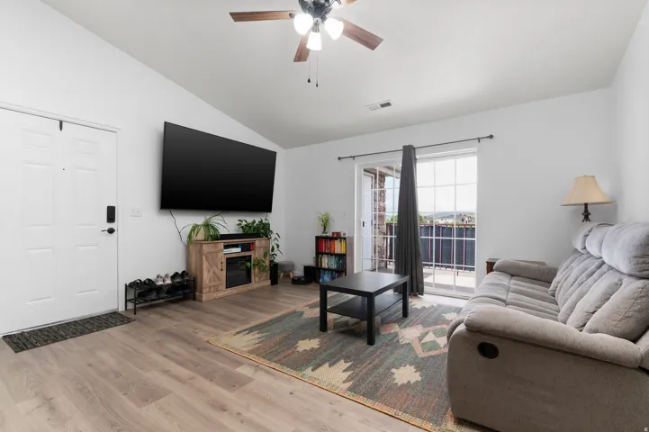 Living area featuring vaulted ceilings, wood-finish flooring, a ceiling fan with light, and a glass sliding door opening to an exterior space