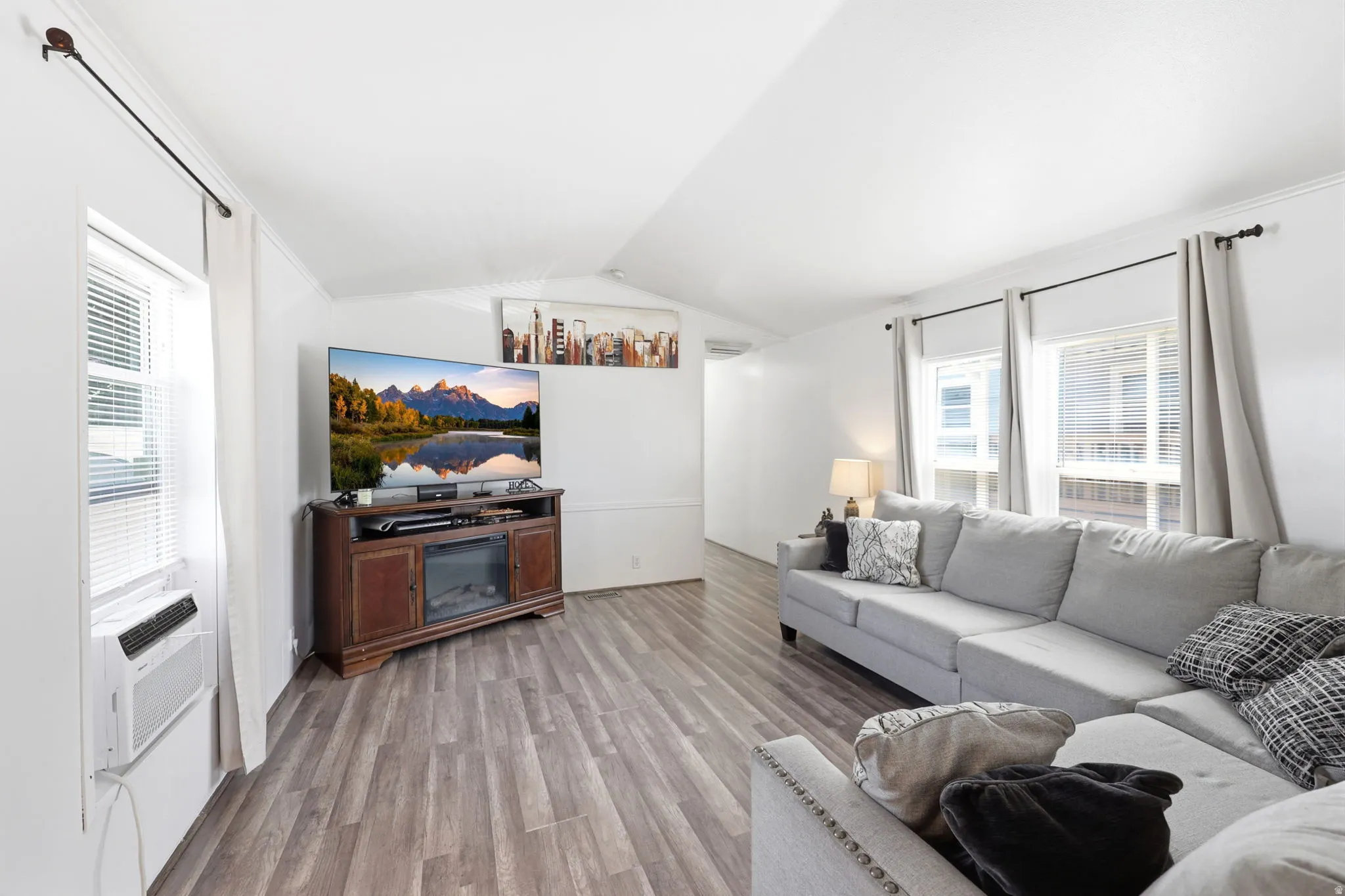 Open-concept living area featuring wood-finish flooring, white walls, and multiple windows with blinds