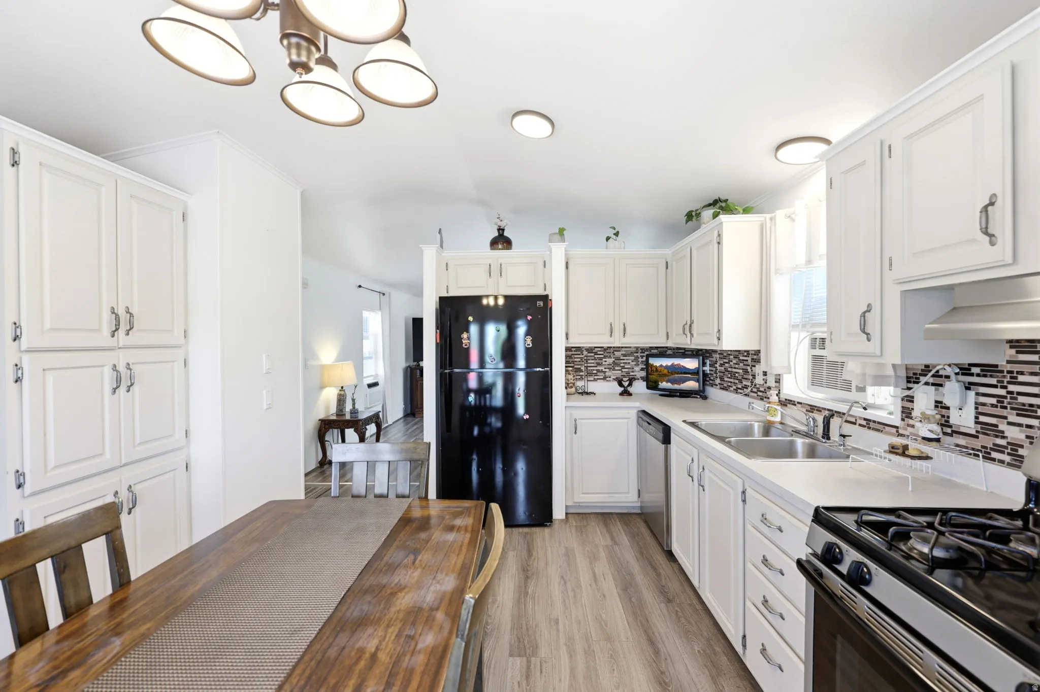 Bright kitchen featuring wood-finish flooring, white cabinetry, a dual basin sink, a mosaic tile backsplash, and a black appliance suite
