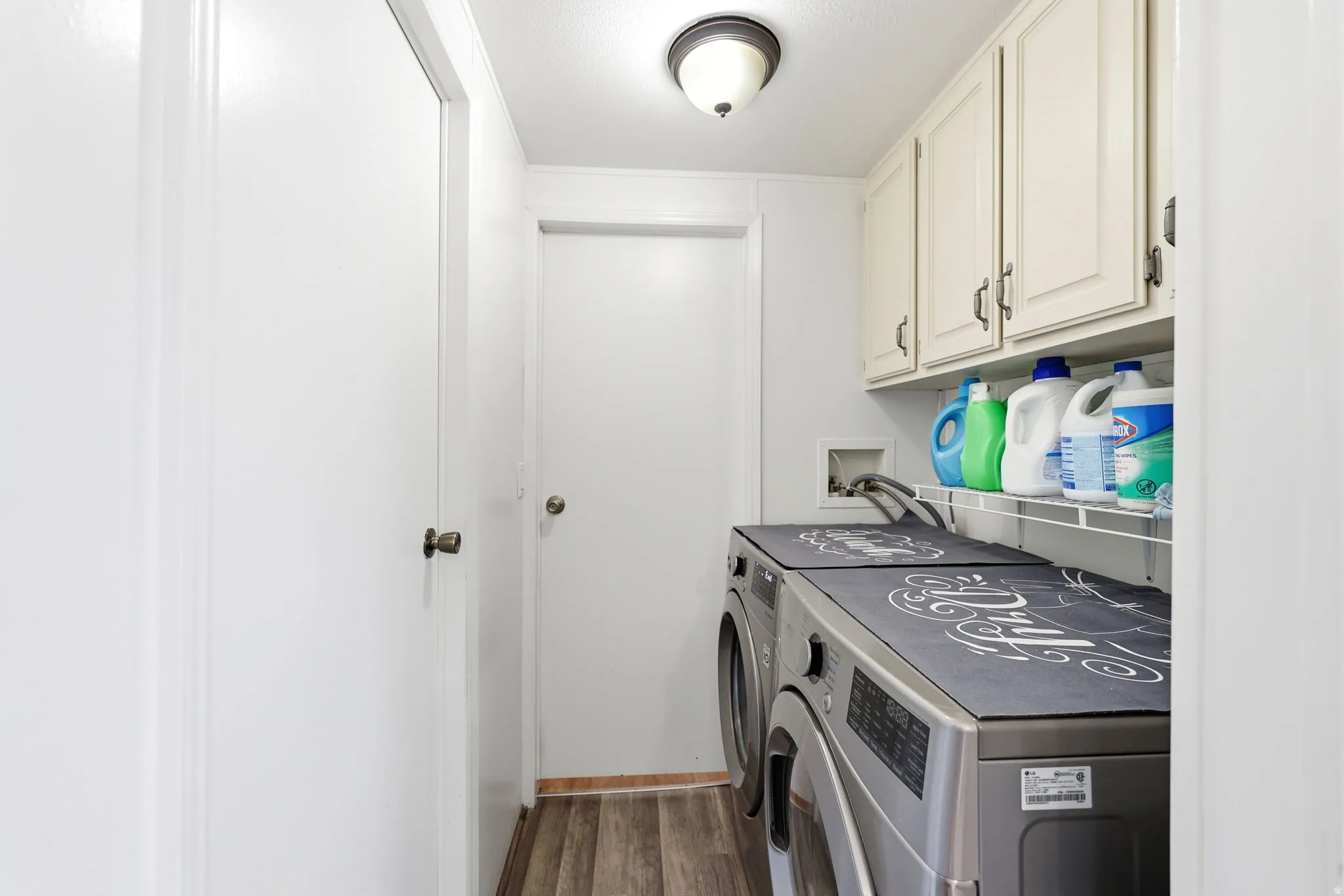 Dedicated laundry area featuring overhead cabinetry, a tiled backsplash, and wood-finish flooring