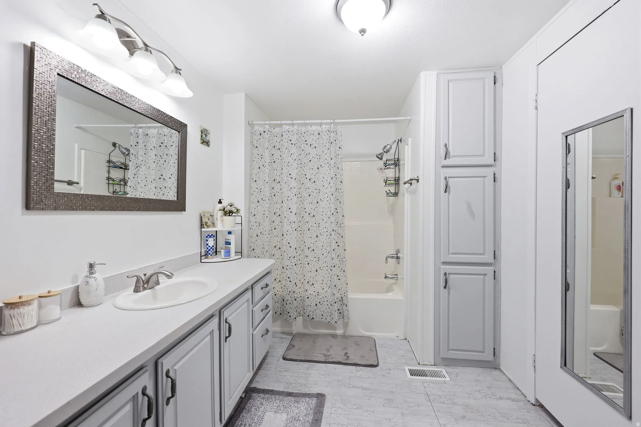 Full bathroom featuring a single vanity with a white countertop and gray cabinetry, a tub/shower combination, and built-in storage cabinets