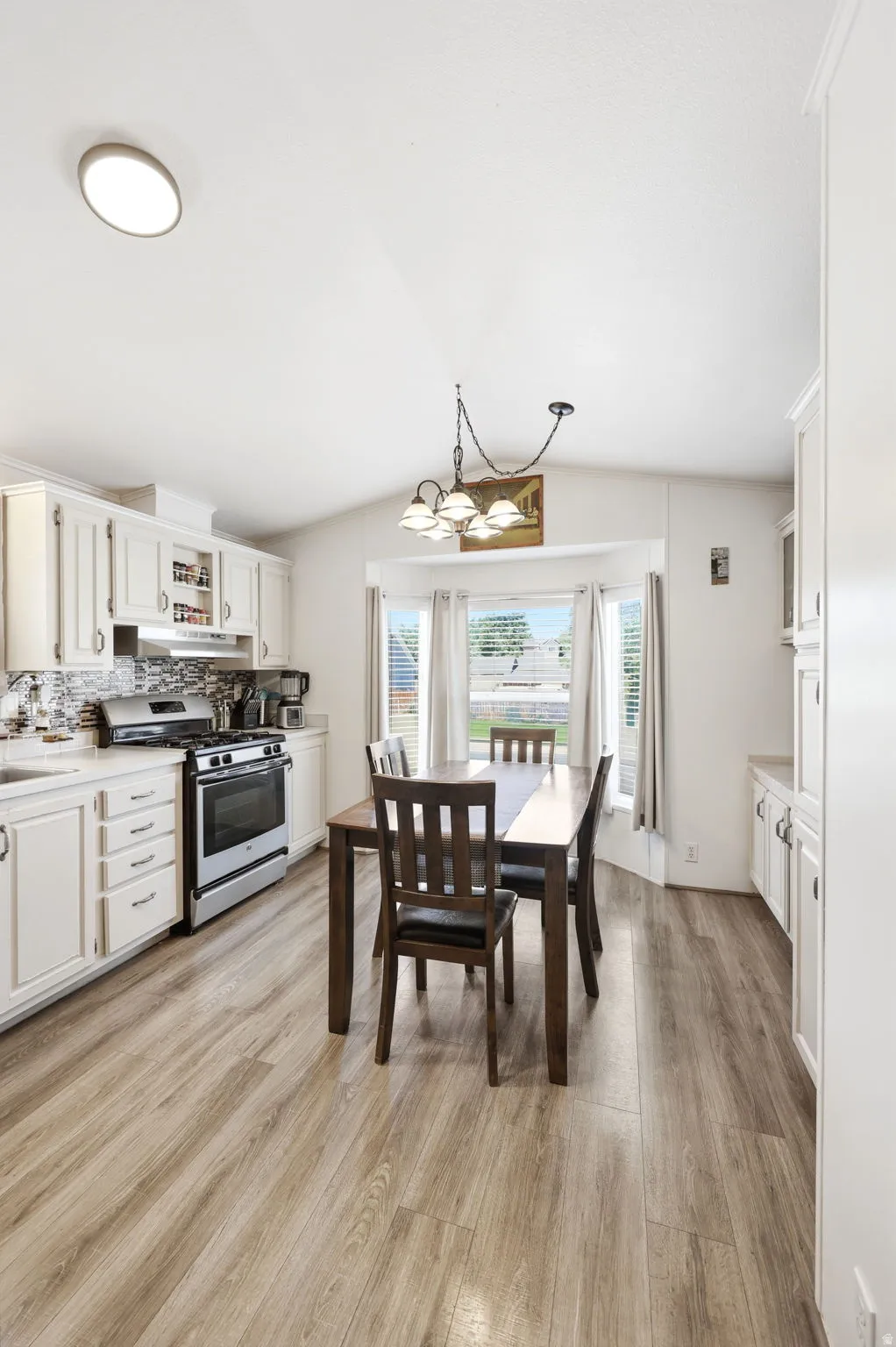 Kitchen and dining area featuring wood-finish flooring, white cabinetry, stainless steel range, and a tiled backsplash