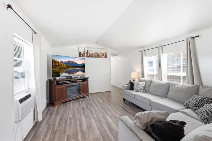 Open-concept living area featuring wood-finish flooring, white walls, and multiple windows with blinds