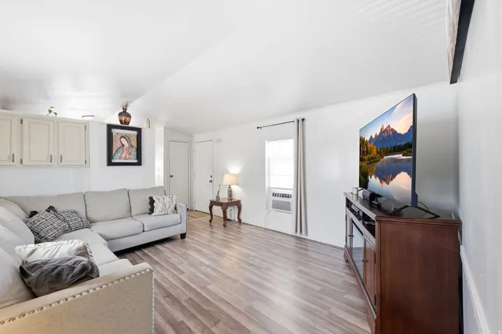 Open-concept living space with wood-finish flooring, white walls, and bright natural light