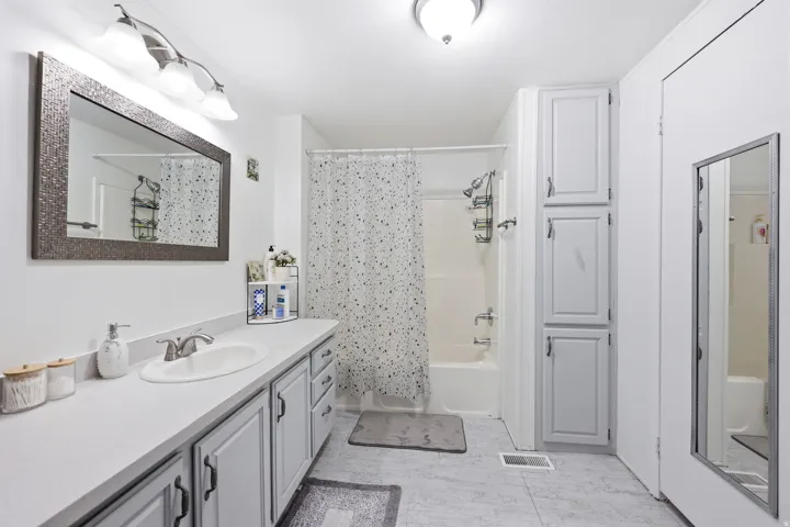 Full bathroom featuring a single vanity with a white countertop and gray cabinetry, a tub/shower combination, and built-in storage cabinets
