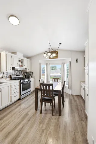 Kitchen and dining area featuring wood-finish flooring, white cabinetry, stainless steel range, and a tiled backsplash