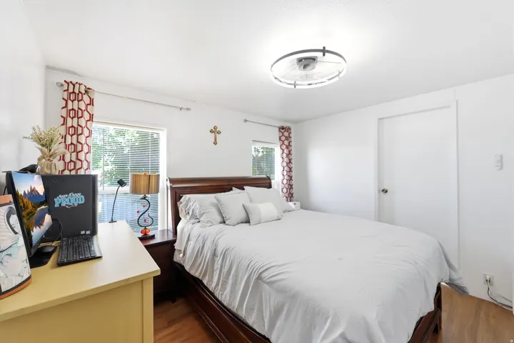 Bedroom featuring two windows with blinds, a ceiling-mounted light fixture, and wood-finish flooring