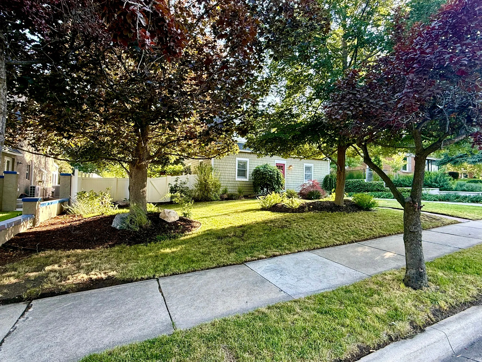 Expansive front yard featuring mature trees, landscaped planting beds, and a concrete sidewalk