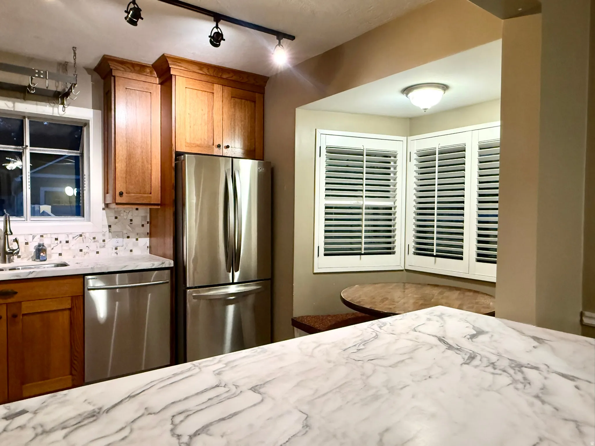 Kitchen featuring a large island with a marbled countertop, stainless steel appliances, wood cabinetry, and a mosaic tile backsplash