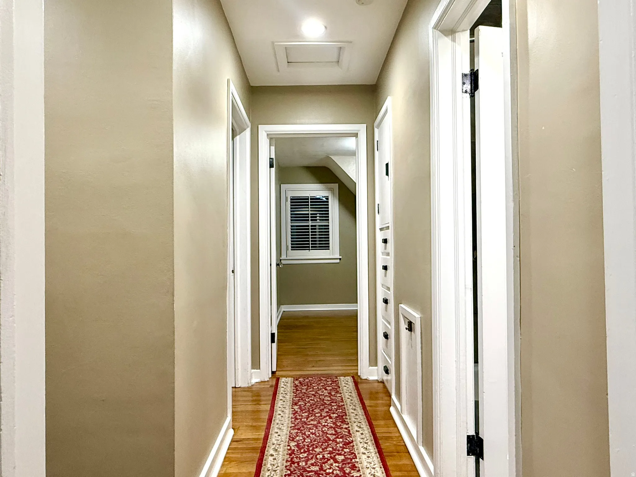 Hallway  between Bedrooms & Bathroom featuring wood-finish flooring, light tan walls, white trim, and a ceiling access panel