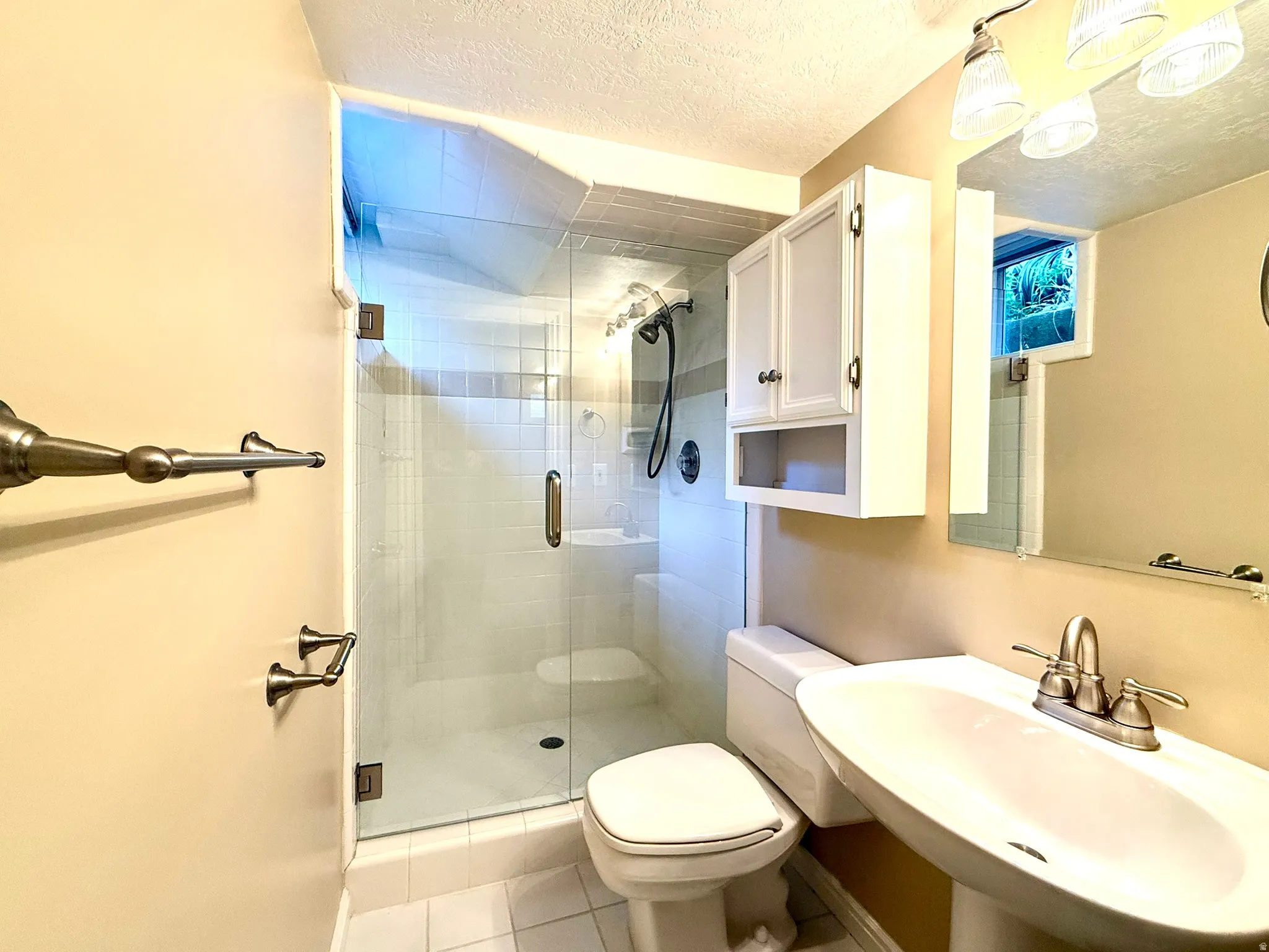 Bathroom featuring a glass-enclosed shower, pedestal sink, wall-mounted storage cabinet, and tiled flooring
