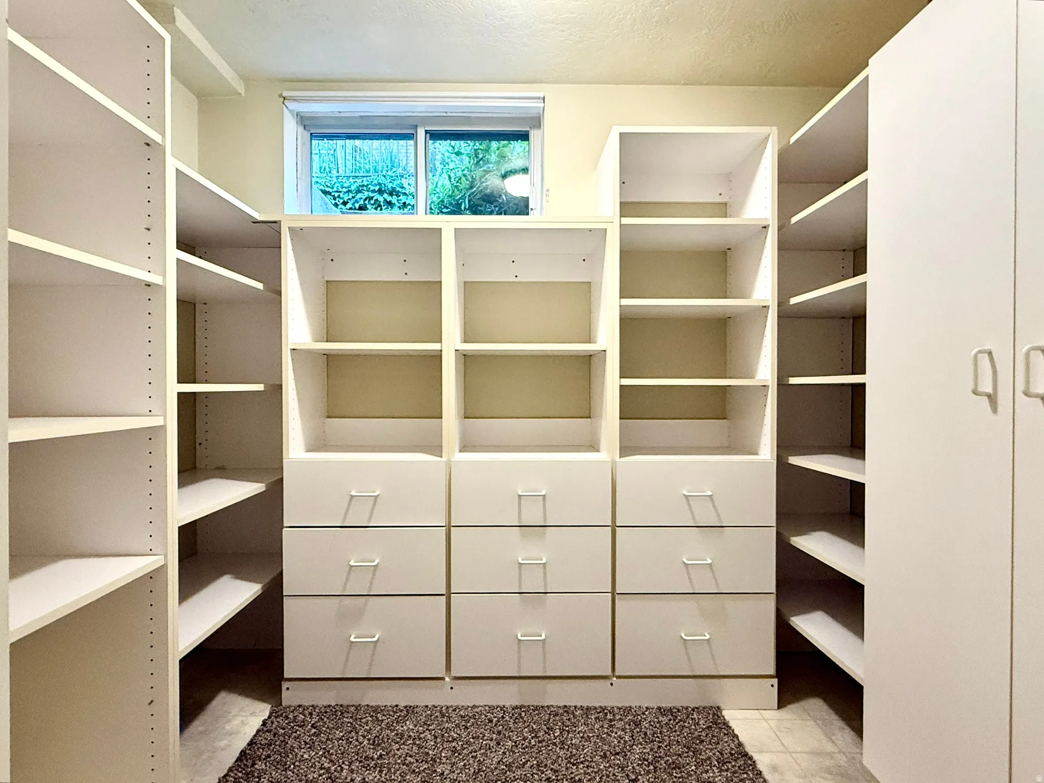 Storage Room Custom white built-in shelving with adjustable shelves, integrated drawers, and a window providing natural light