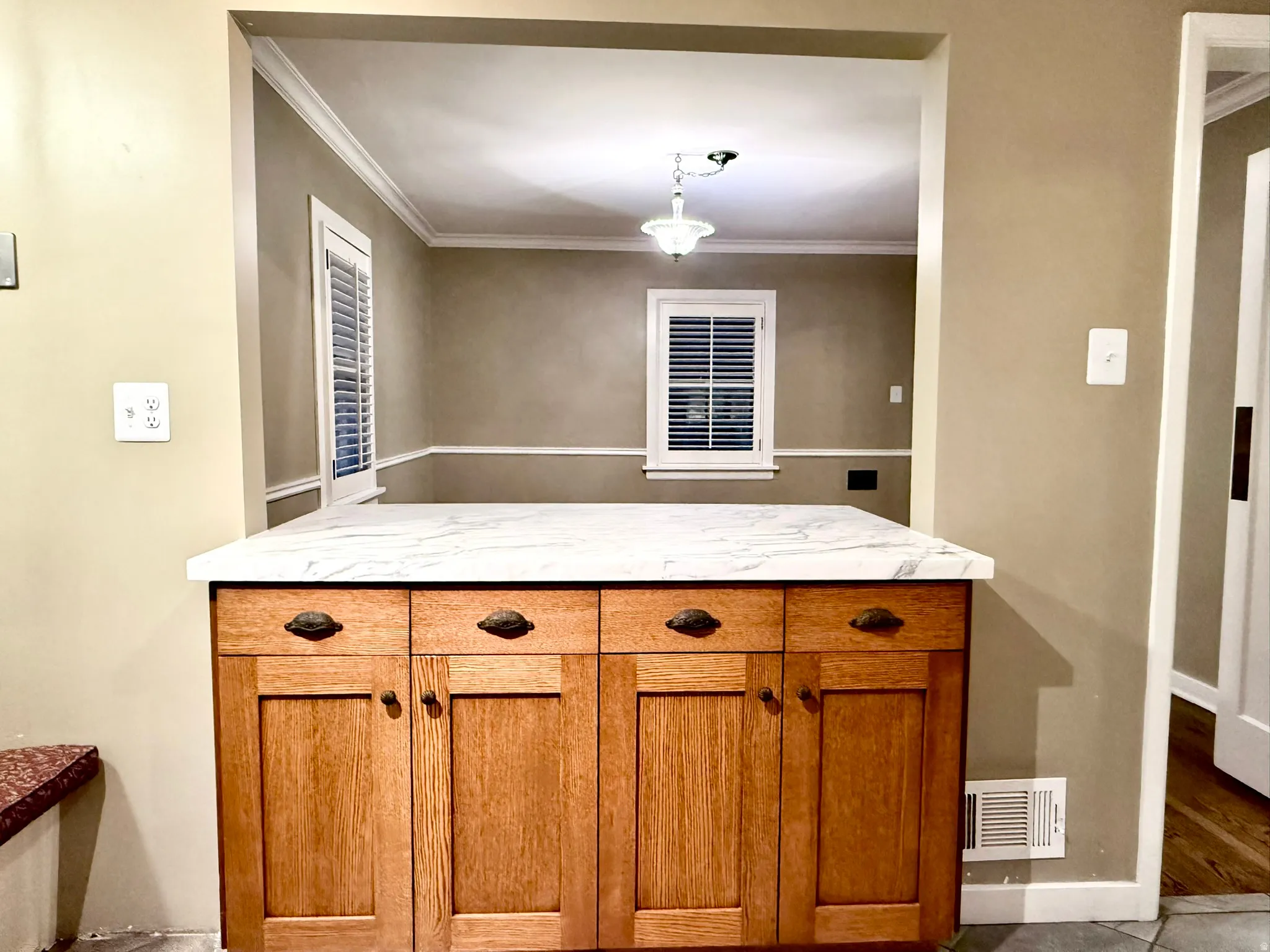Wood-finish cabinetry with a white marble-look countertop, featuring a pass-through opening to an adjacent room