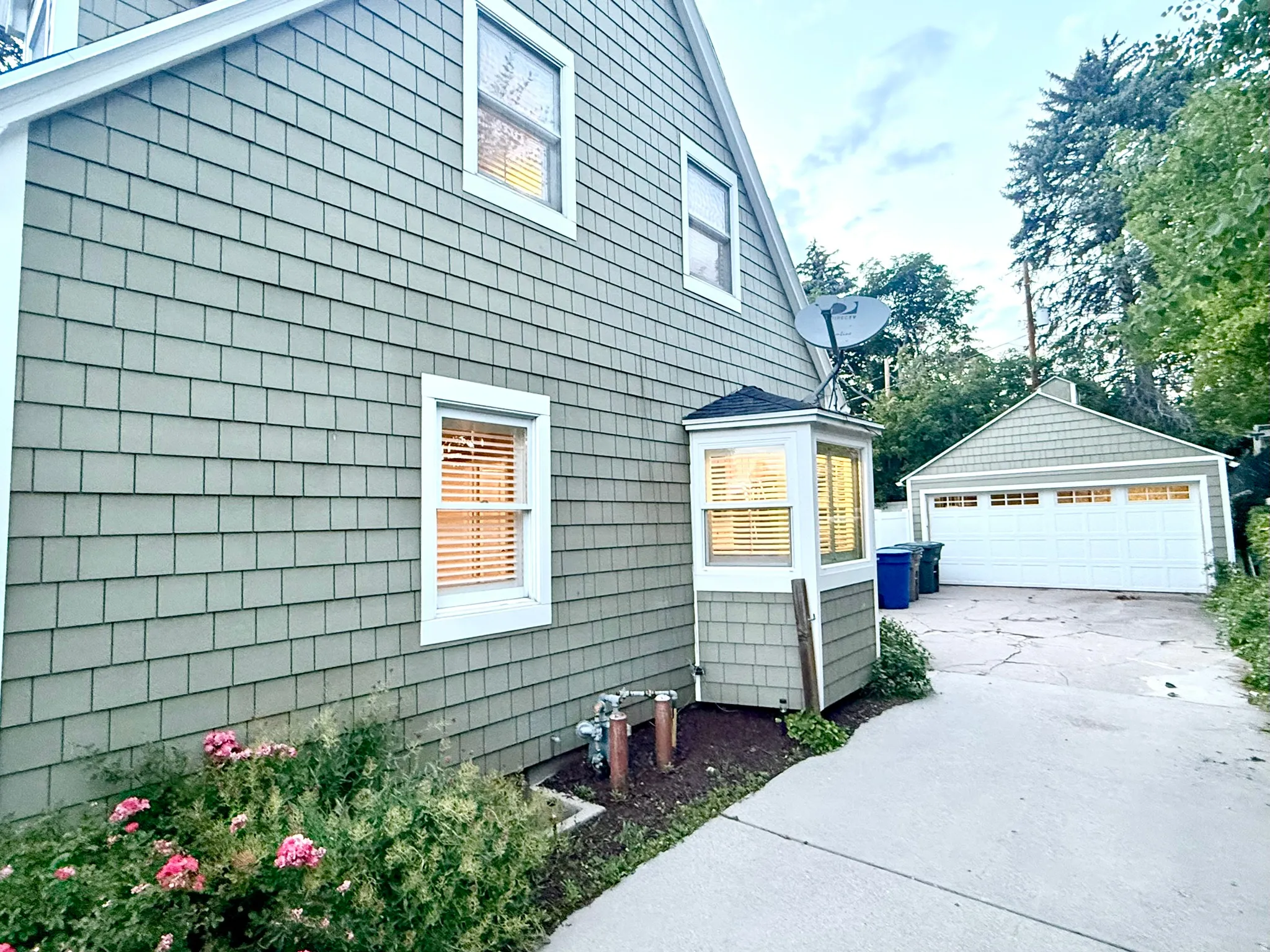 Shingle-sided exterior featuring a bay window, white-trimmed windows, and a detached two-car garage with a white panel door