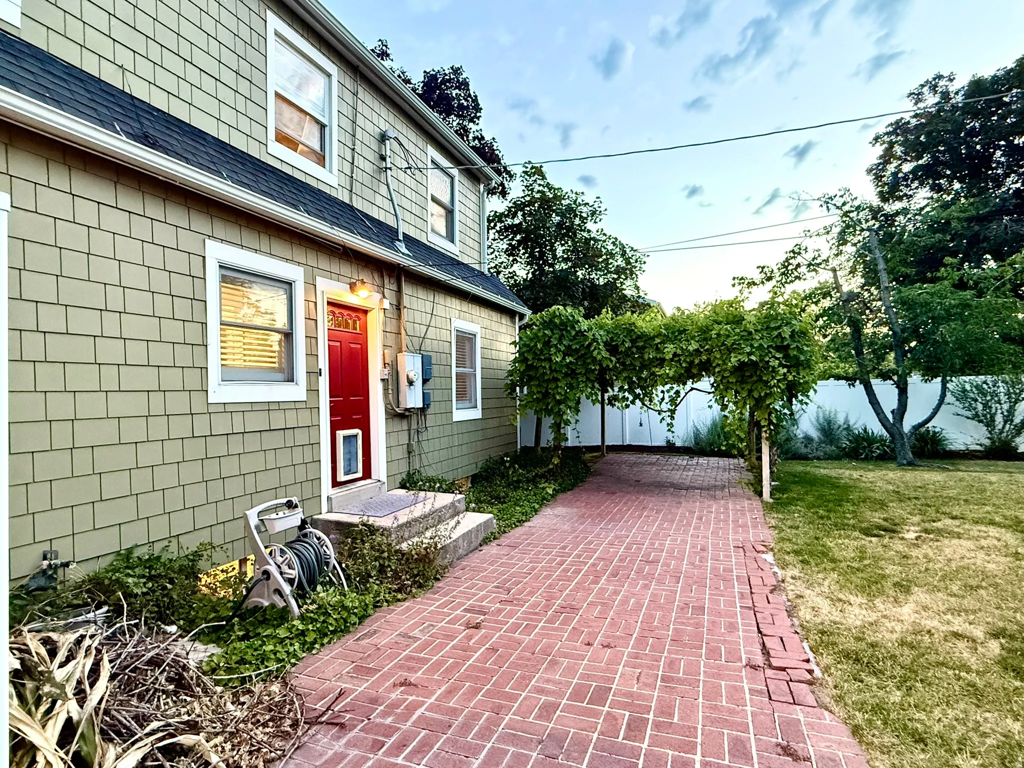 Two-story residence featuring light green shingle siding, a dark roof, and a vibrant red entry door