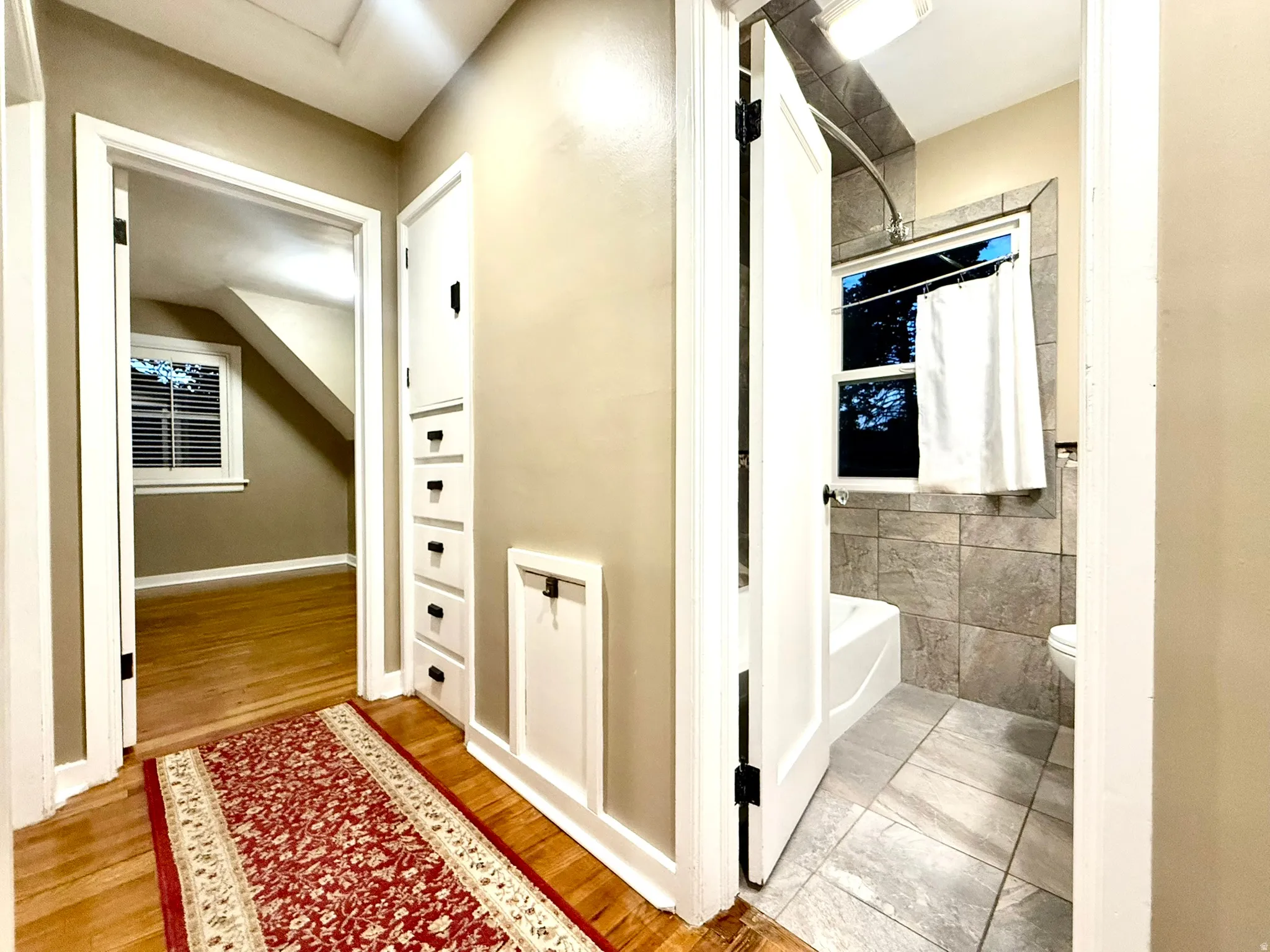 Hallway with Built in cabinets Well-appointed bathroom featuring a white bathtub, tiled shower surround, and tiled flooring