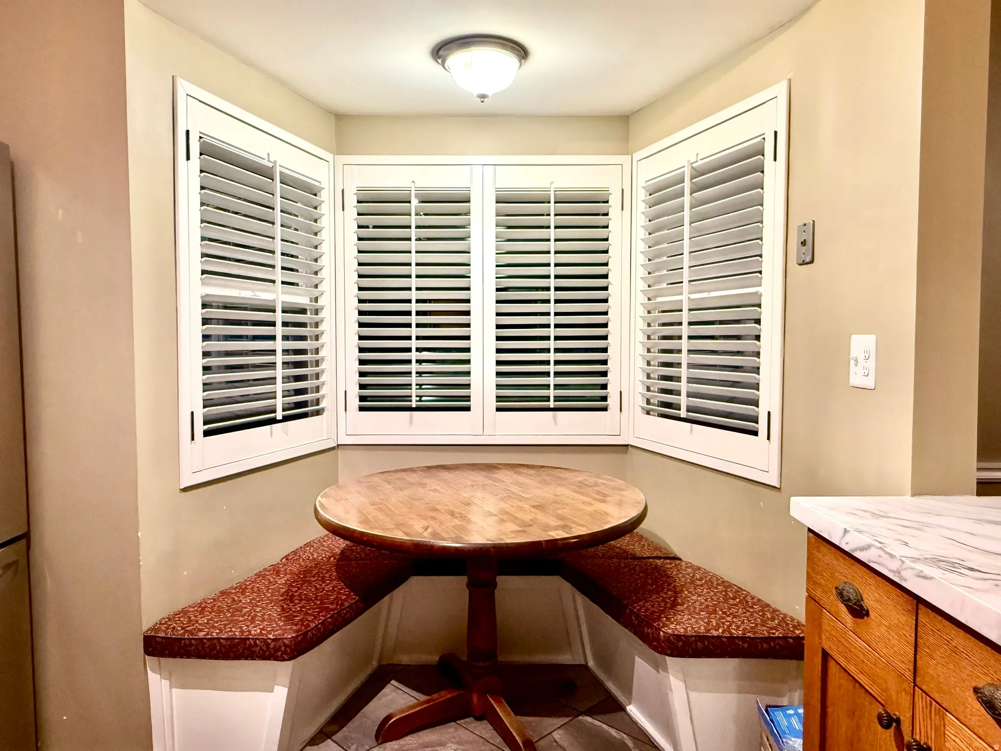 Built-in corner bench seating with patterned cushions, complemented by bay windows featuring white plantation shutters