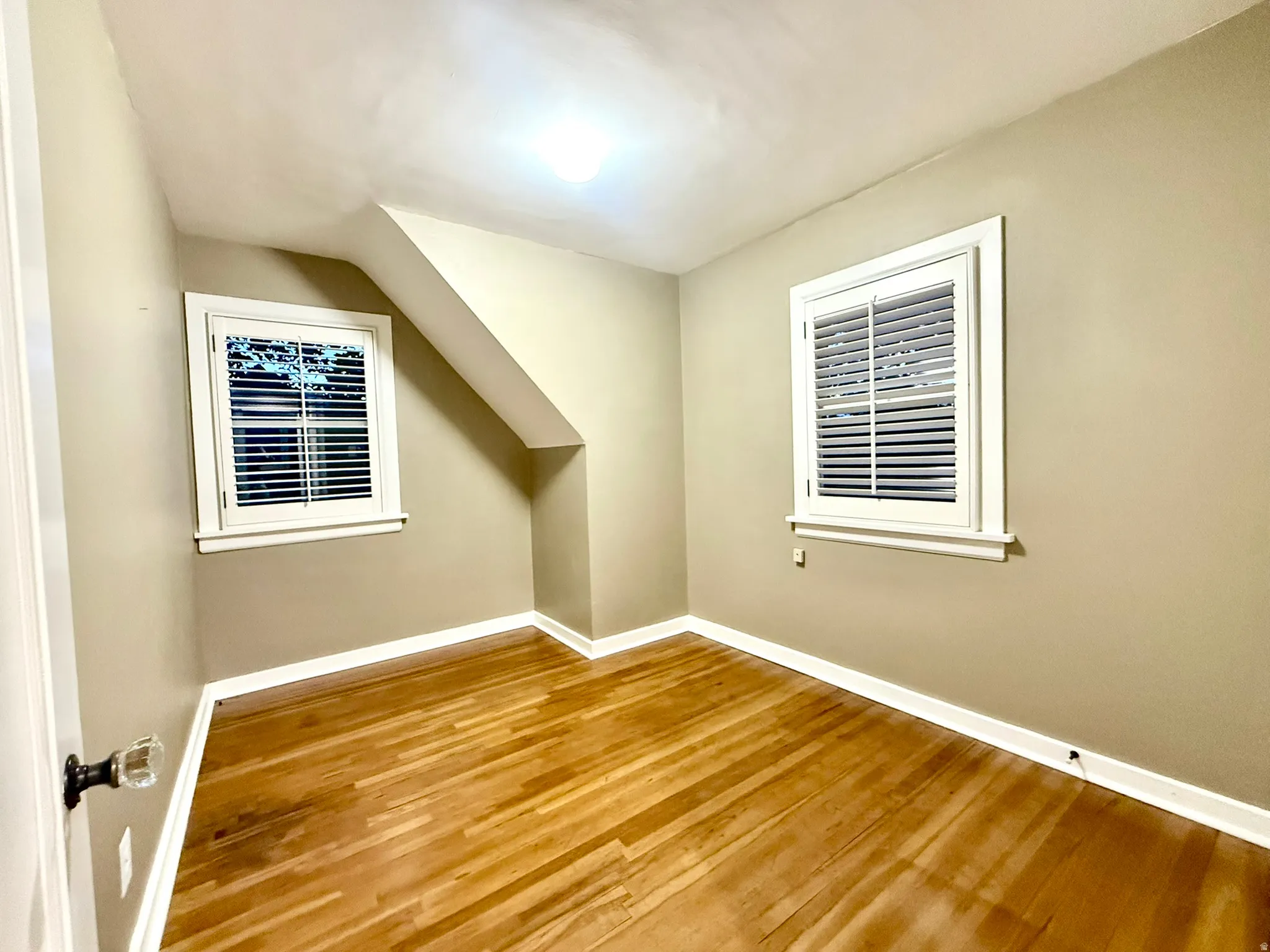 Bedroom #3  featuring wood-finish flooring, two windows with white louvered shutters, and an angled ceiling detail