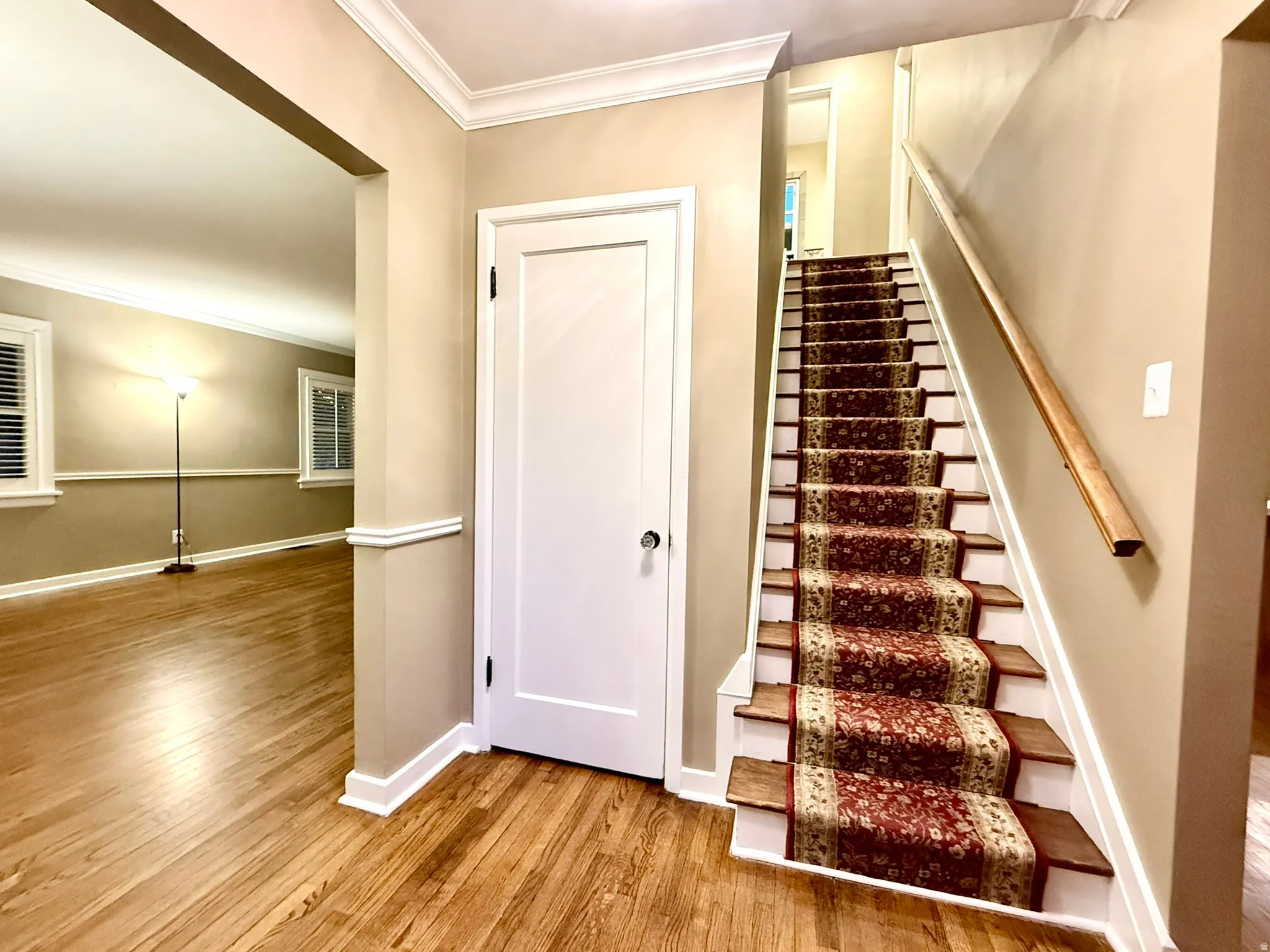 Entryway featuring wood-finish flooring, a carpeted staircase with a wooden handrail, and an arched doorway leading to an additional space