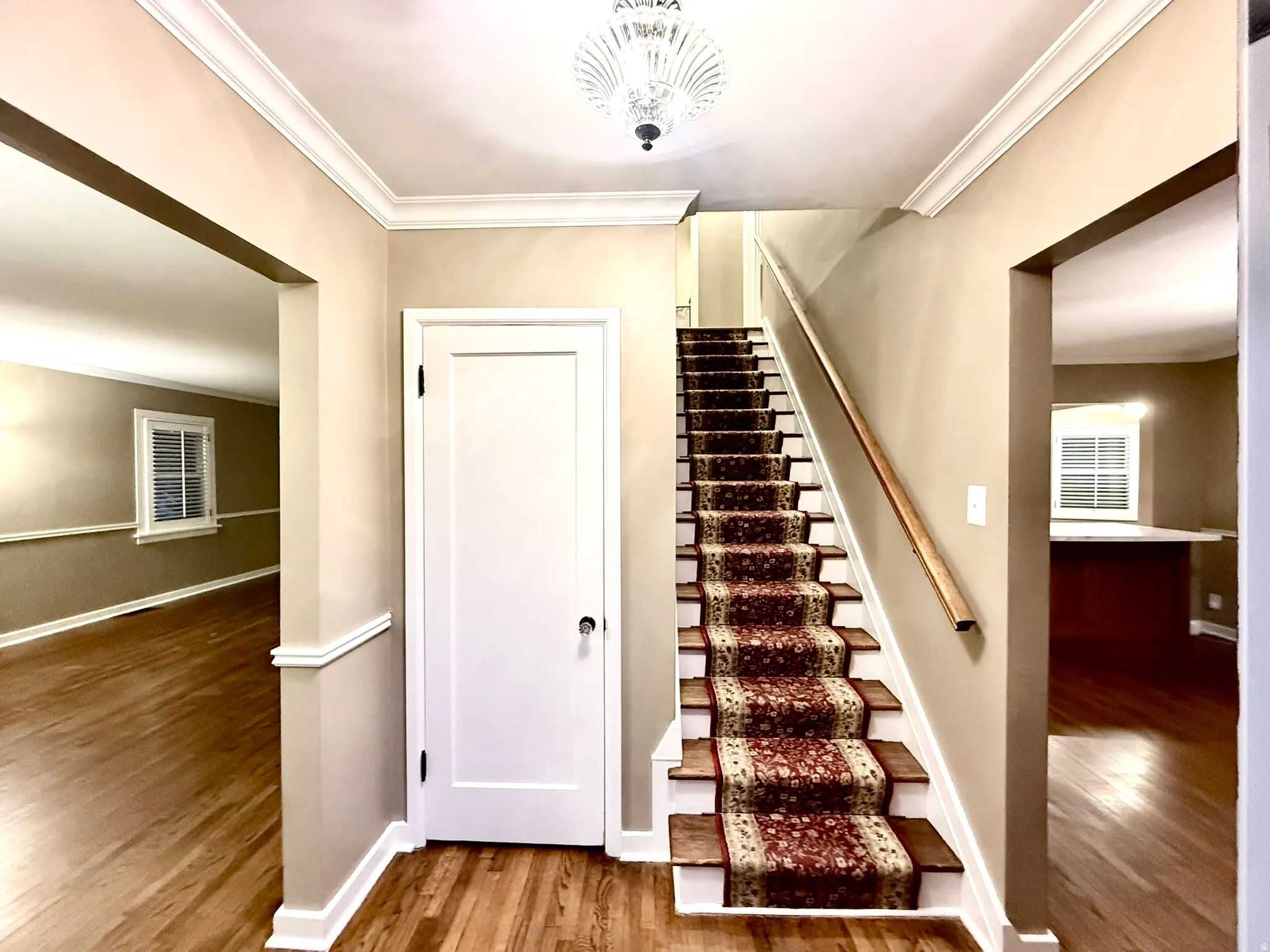 Foyer featuring wood-finish flooring, a carpeted staircase with wood handrail, and crown molding