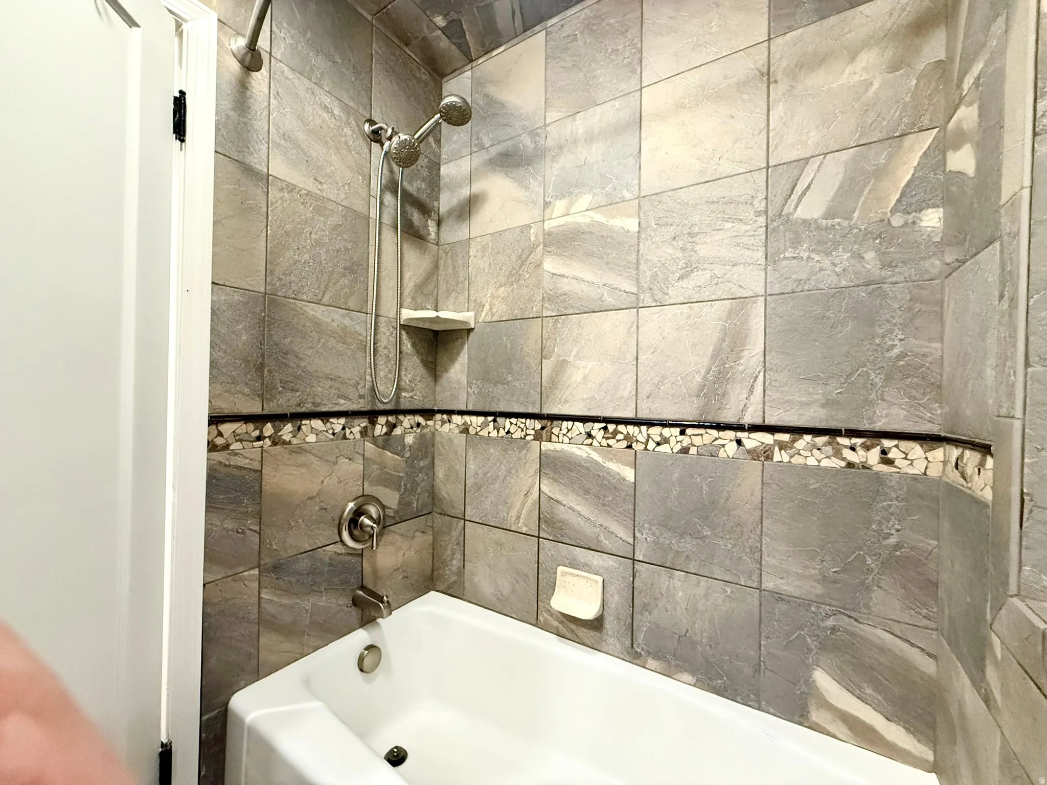 UL Bathtub and shower combination featuring a stone tile surround with a mosaic accent band